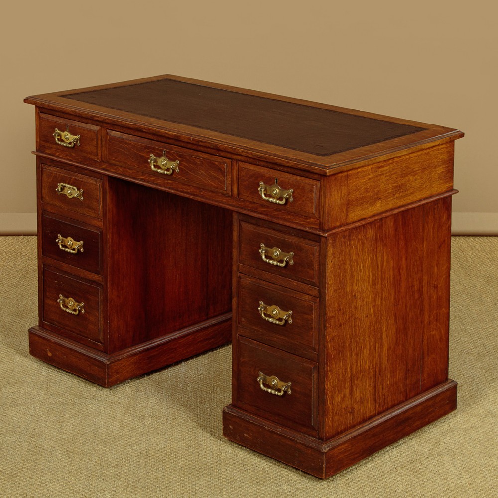 A late Victorian oak pedestal desk featuring a dark brown leather writing top, nine drawers with brass handles, and a solid plinth base.