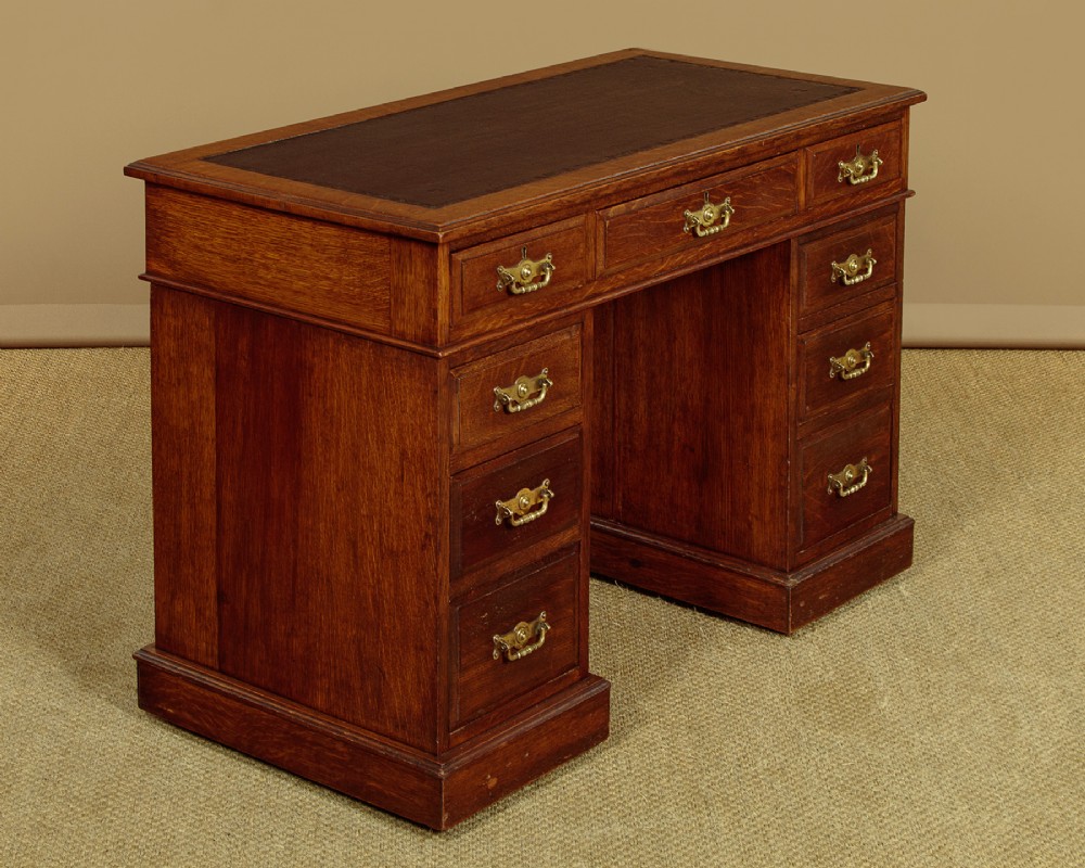A late Victorian oak pedestal desk featuring a dark brown leather writing top, nine drawers with brass handles, and a solid plinth base. View II