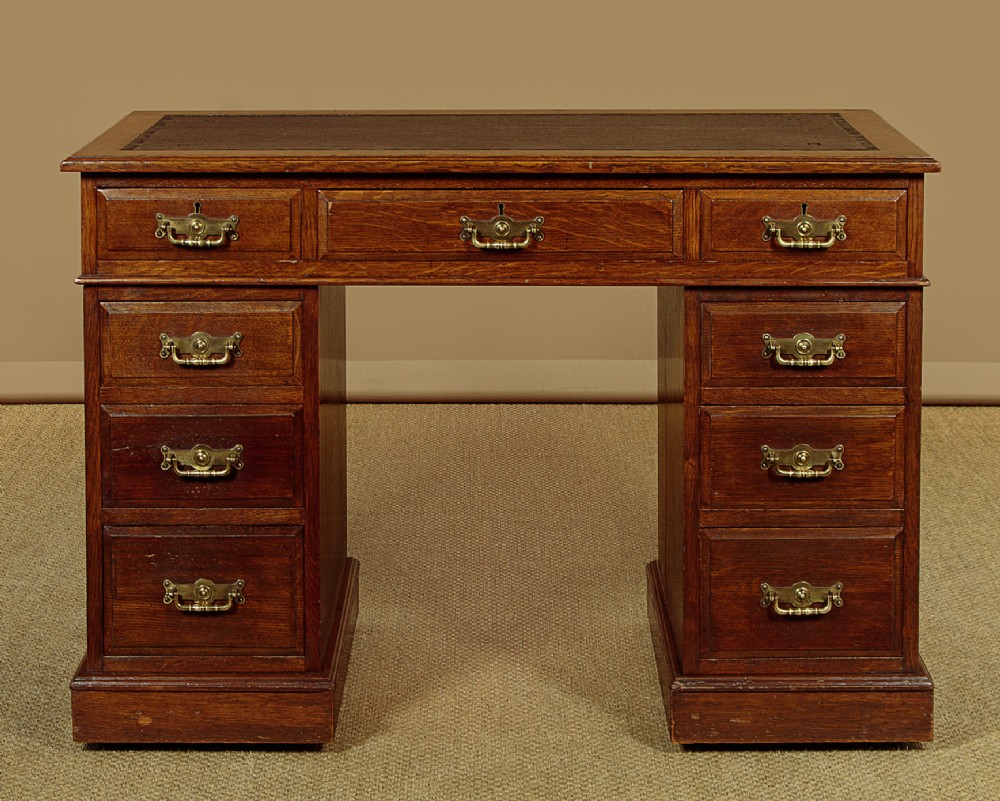 A late Victorian oak pedestal desk featuring a dark brown leather writing top, nine drawers with brass handles, and a solid plinth base. View III