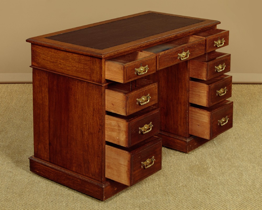 A late Victorian oak pedestal desk featuring a dark brown leather writing top, nine drawers with brass handles, and a solid plinth base. View IV