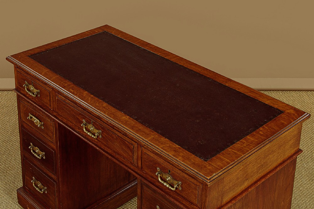 A late Victorian oak pedestal desk featuring a dark brown leather writing top, nine drawers with brass handles, and a solid plinth base. View V