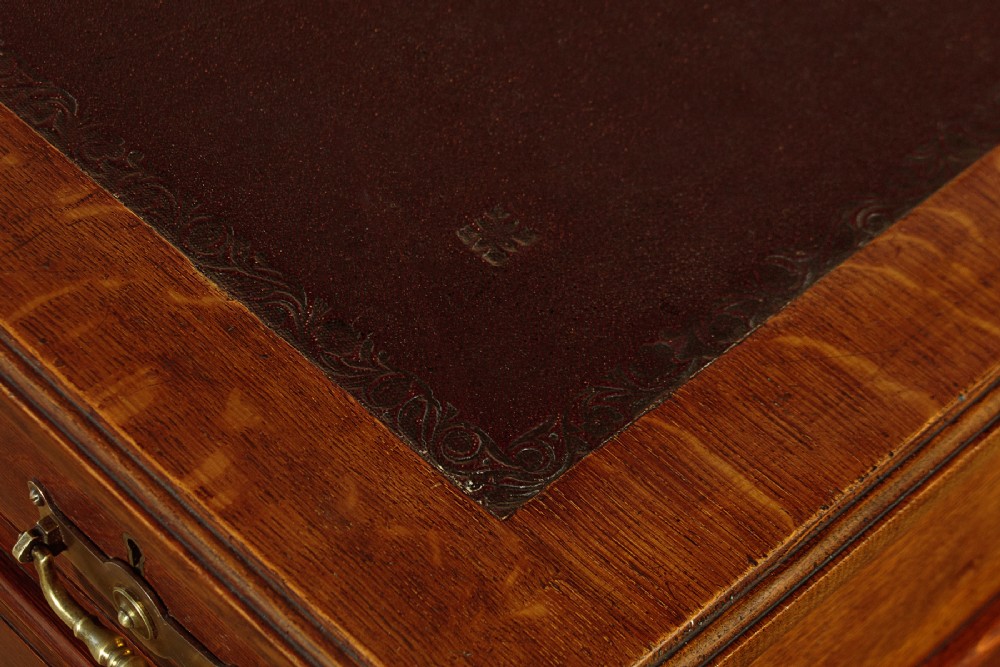 A late Victorian oak pedestal desk featuring a dark brown leather writing top, nine drawers with brass handles, and a solid plinth base. View VI