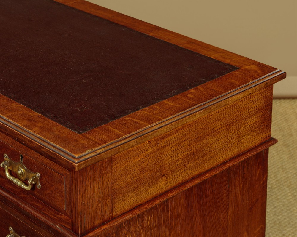A late Victorian oak pedestal desk featuring a dark brown leather writing top, nine drawers with brass handles, and a solid plinth base. View VII