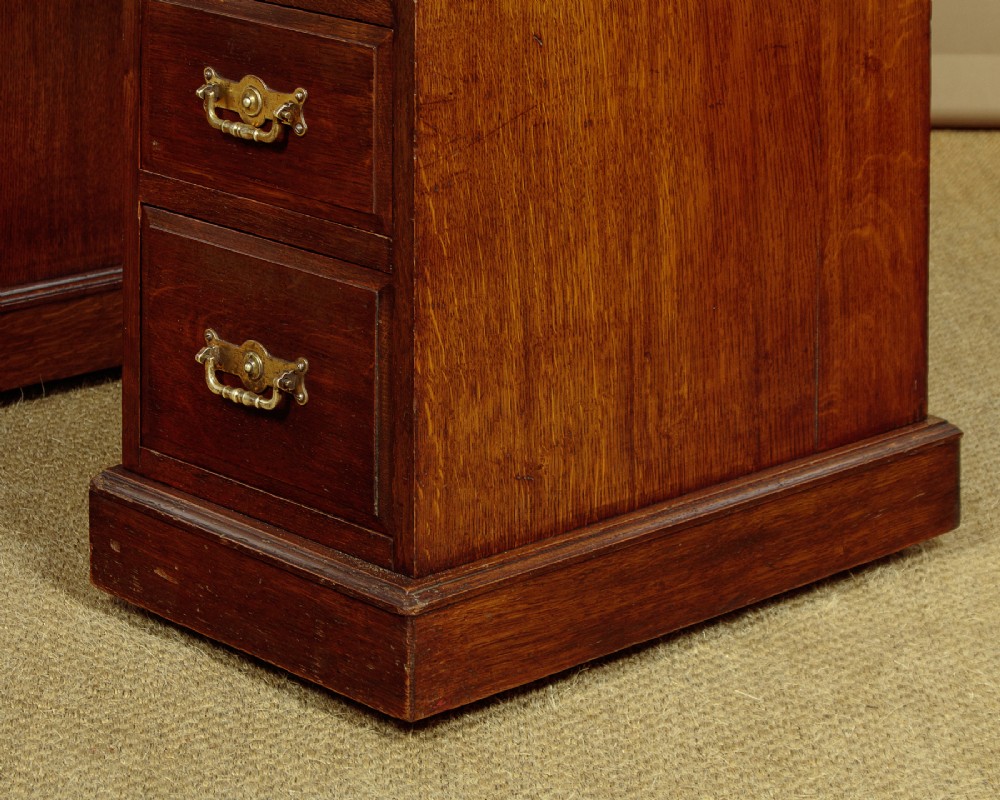 A late Victorian oak pedestal desk featuring a dark brown leather writing top, nine drawers with brass handles, and a solid plinth base. View IX