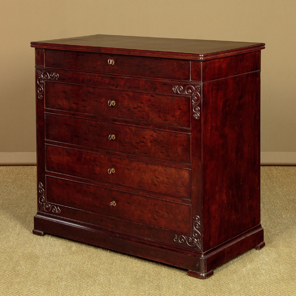 A mid-19th century French Louis Philippe mahogany chest of drawers featuring five stacked drawers, polished dark timber finish, brass keyhole escutcheons, and foliate carvings framing the corners.