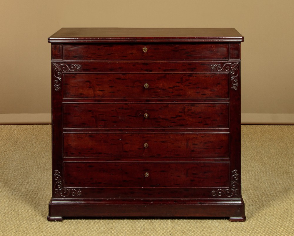 A mid-19th century French Louis Philippe mahogany chest of drawers featuring five stacked drawers, polished dark timber finish, brass keyhole escutcheons, and foliate carvings framing the corners. View II