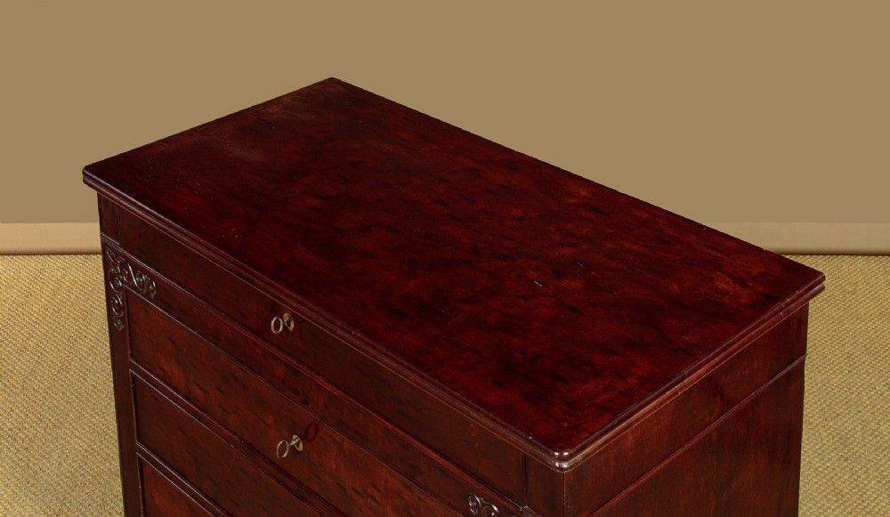A mid-19th century French Louis Philippe mahogany chest of drawers featuring five stacked drawers, polished dark timber finish, brass keyhole escutcheons, and foliate carvings framing the corners. View IV
