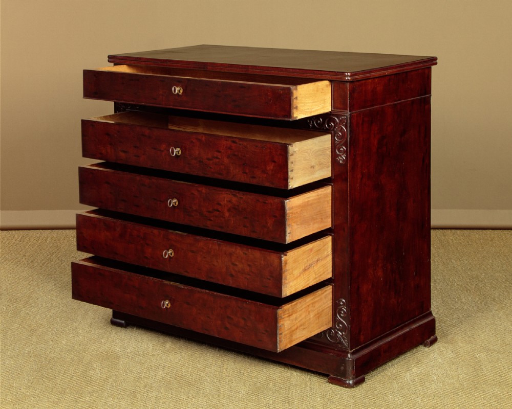 A mid-19th century French Louis Philippe mahogany chest of drawers featuring five stacked drawers, polished dark timber finish, brass keyhole escutcheons, and foliate carvings framing the corners. View V