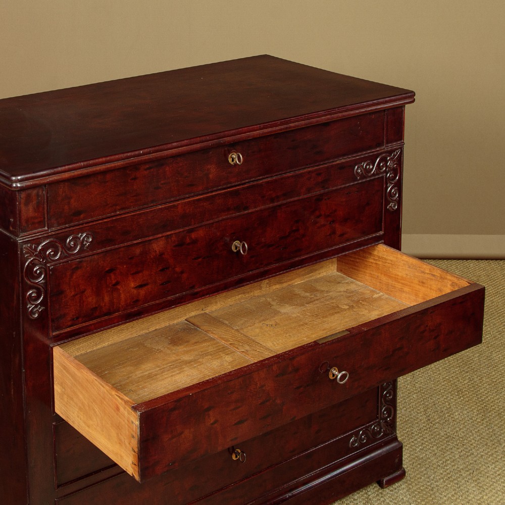 A mid-19th century French Louis Philippe mahogany chest of drawers featuring five stacked drawers, polished dark timber finish, brass keyhole escutcheons, and foliate carvings framing the corners. View VI
