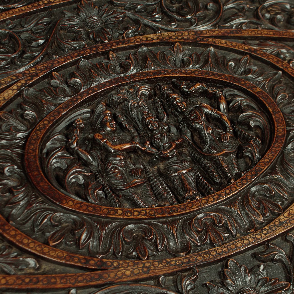 An oval dark hardwood Anglo-Indian coffee table featuring intricate top carvings and four legs sculpted as mythological beasts with inset white teeth. View III