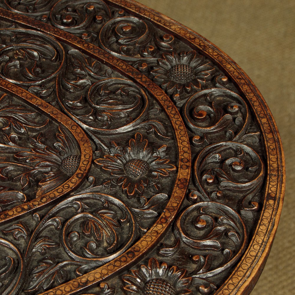 An oval dark hardwood Anglo-Indian coffee table featuring intricate top carvings and four legs sculpted as mythological beasts with inset white teeth. View IV