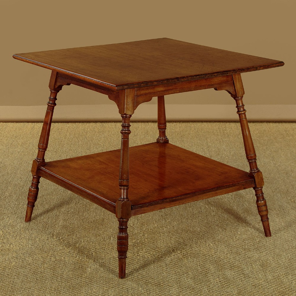 A square low Arts and Crafts style mahogany side table featuring turned splayed legs, a lower shelf, and decorative corner spandrels.