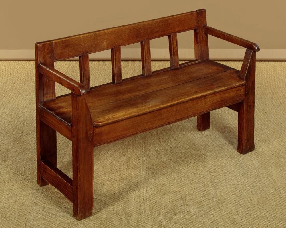 A small antique warm brown oak hall bench featuring a slatted open backrest, straight armrests, and a solid plank seat.