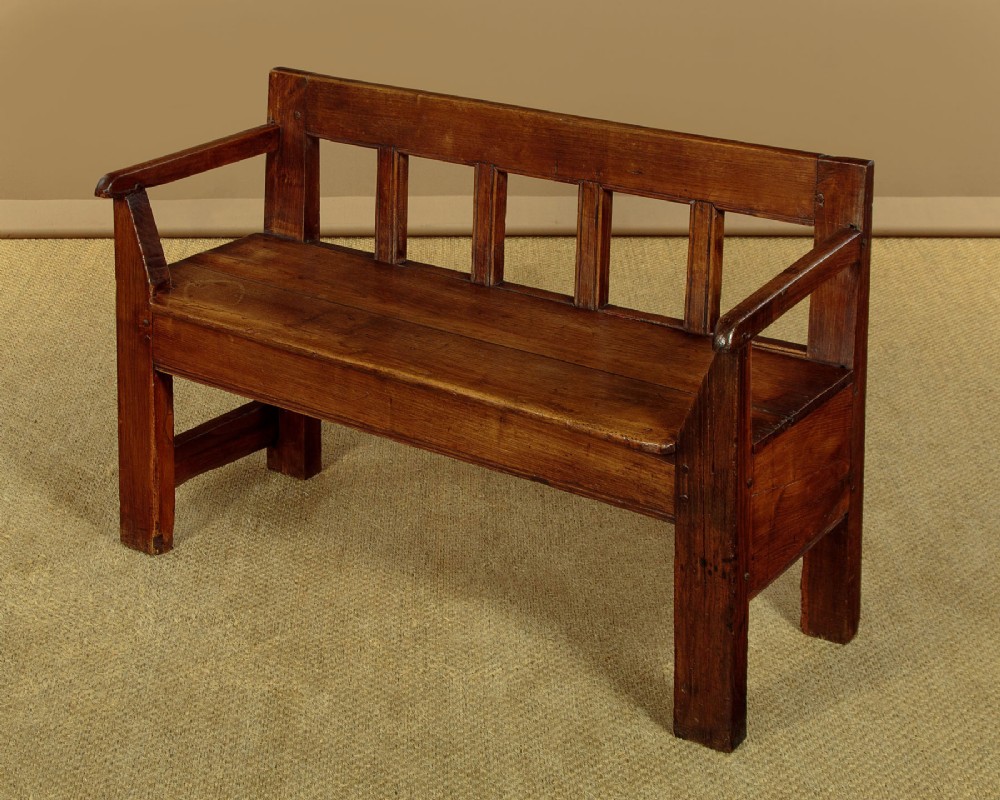 A small antique warm brown oak hall bench featuring a slatted open backrest, straight armrests, and a solid plank seat. View III