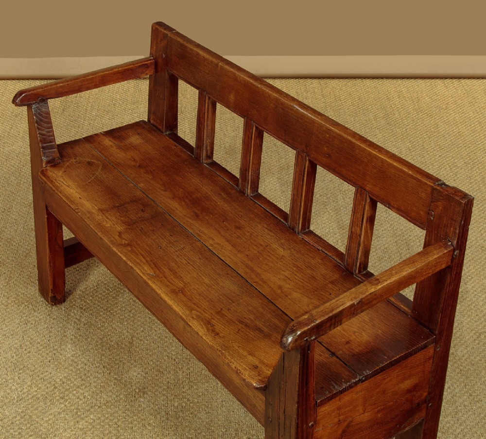 A small antique warm brown oak hall bench featuring a slatted open backrest, straight armrests, and a solid plank seat. View IV