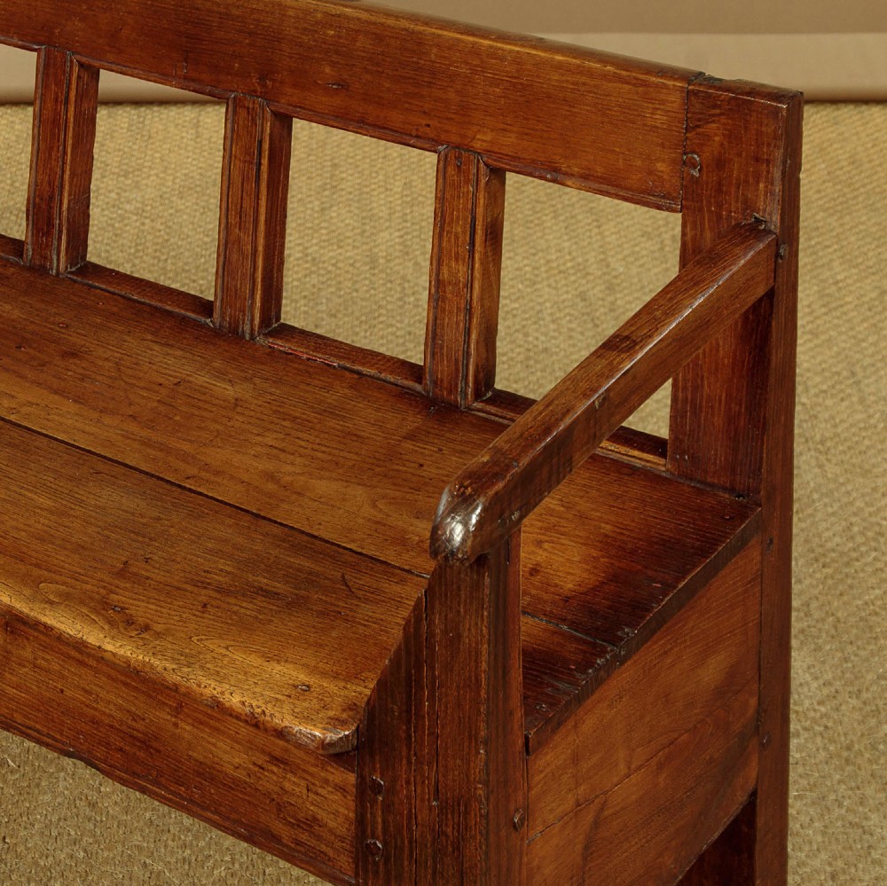 A small antique warm brown oak hall bench featuring a slatted open backrest, straight armrests, and a solid plank seat. View V