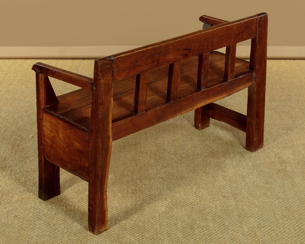 A small antique warm brown oak hall bench featuring a slatted open backrest, straight armrests, and a solid plank seat. View IX