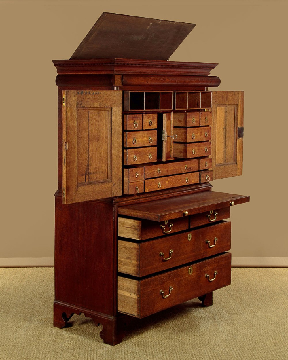 An early 18th-century oak cabinet on chest featuring twin panelled doors opening to internal drawers and pigeonholes above a chest of drawers with brass handles.