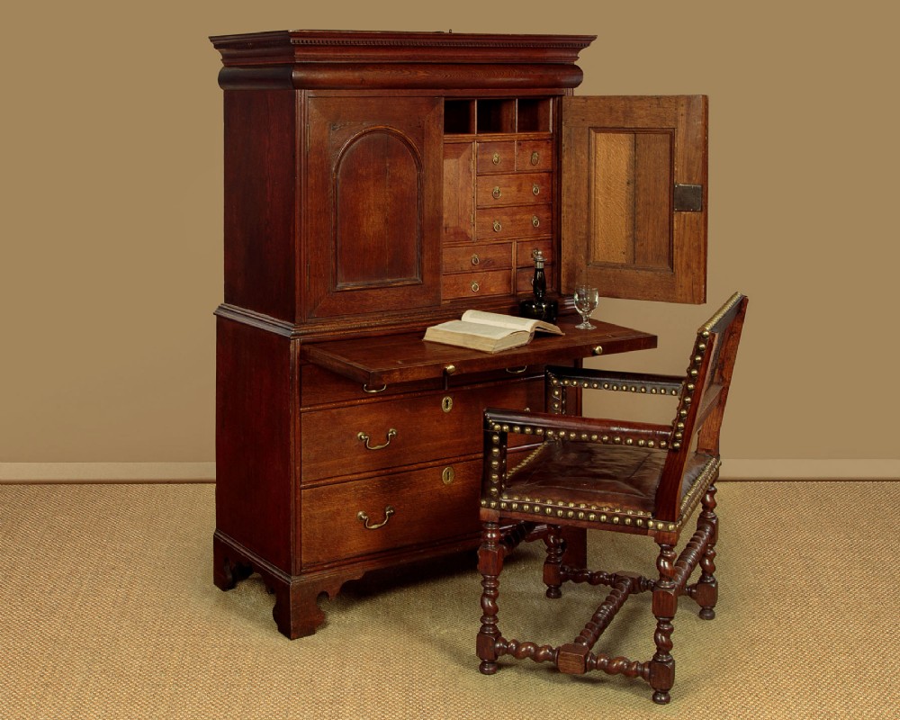 An early 18th-century oak cabinet on chest featuring twin panelled doors opening to internal drawers and pigeonholes above a chest of drawers with brass handles. View II