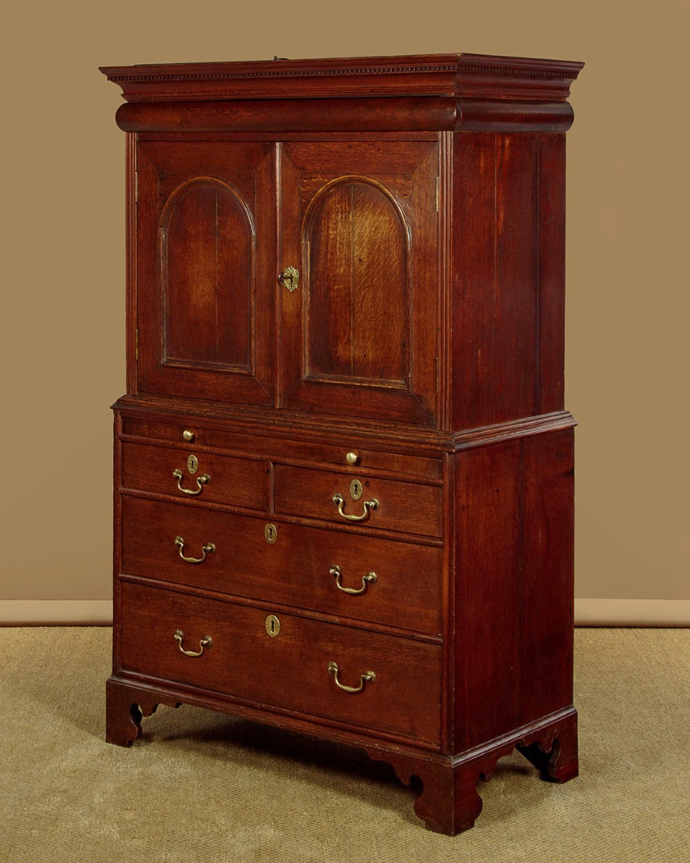 An early 18th-century oak cabinet on chest featuring twin panelled doors opening to internal drawers and pigeonholes above a chest of drawers with brass handles. View IV