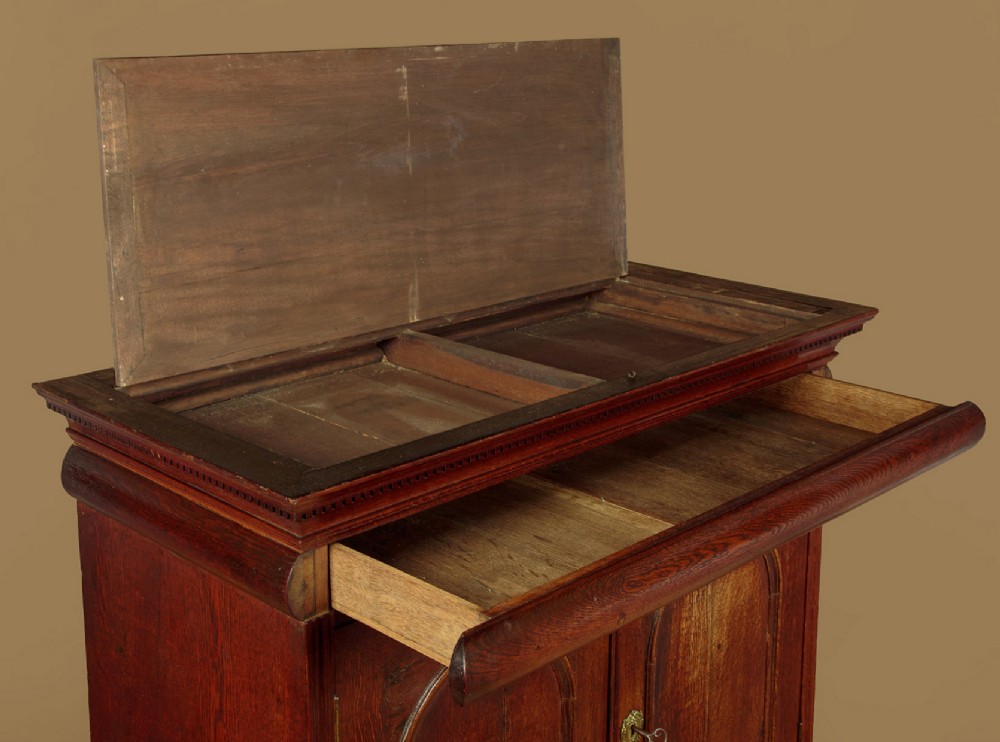 An early 18th-century oak cabinet on chest featuring twin panelled doors opening to internal drawers and pigeonholes above a chest of drawers with brass handles. View V
