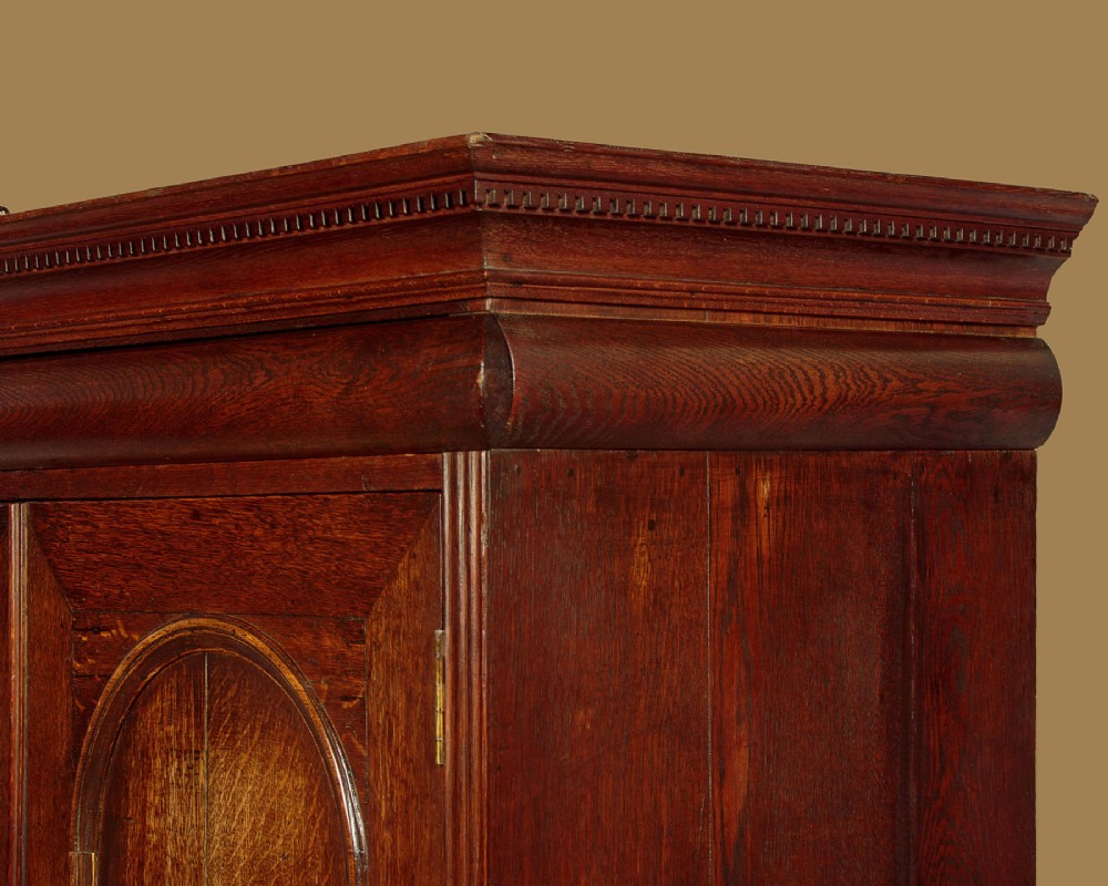 An early 18th-century oak cabinet on chest featuring twin panelled doors opening to internal drawers and pigeonholes above a chest of drawers with brass handles. View VI