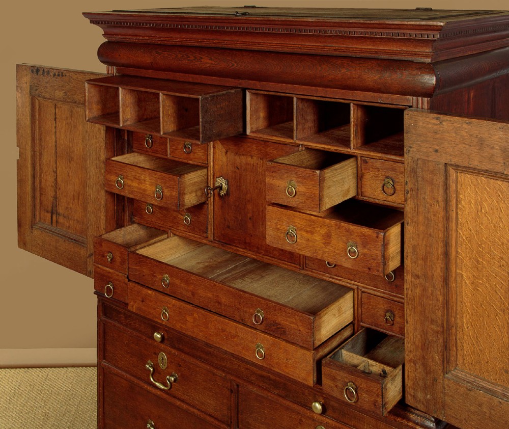 An early 18th-century oak cabinet on chest featuring twin panelled doors opening to internal drawers and pigeonholes above a chest of drawers with brass handles. View VII