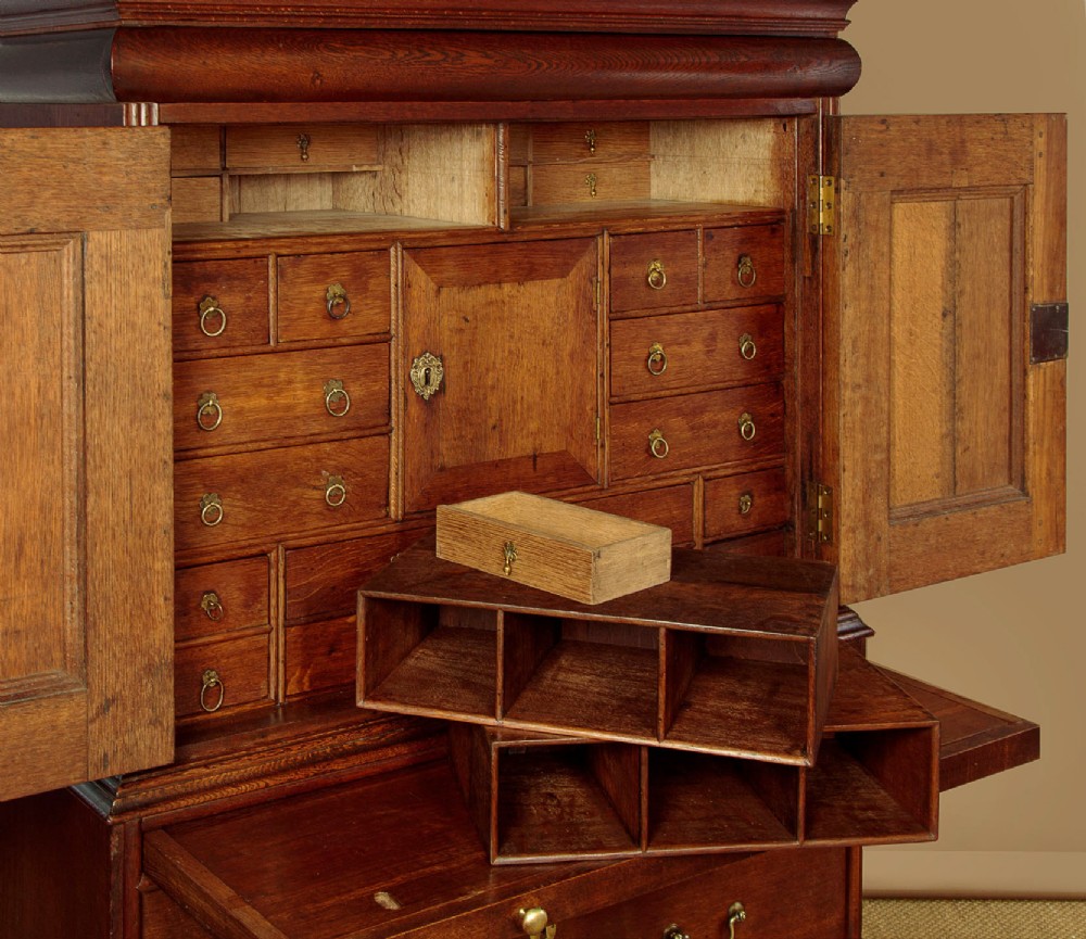 An early 18th-century oak cabinet on chest featuring twin panelled doors opening to internal drawers and pigeonholes above a chest of drawers with brass handles. View VIII