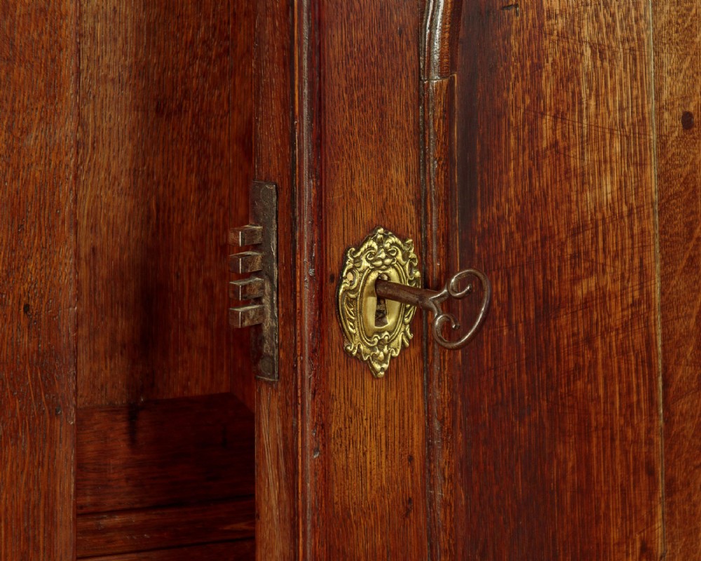 An early 18th-century oak cabinet on chest featuring twin panelled doors opening to internal drawers and pigeonholes above a chest of drawers with brass handles. View XI