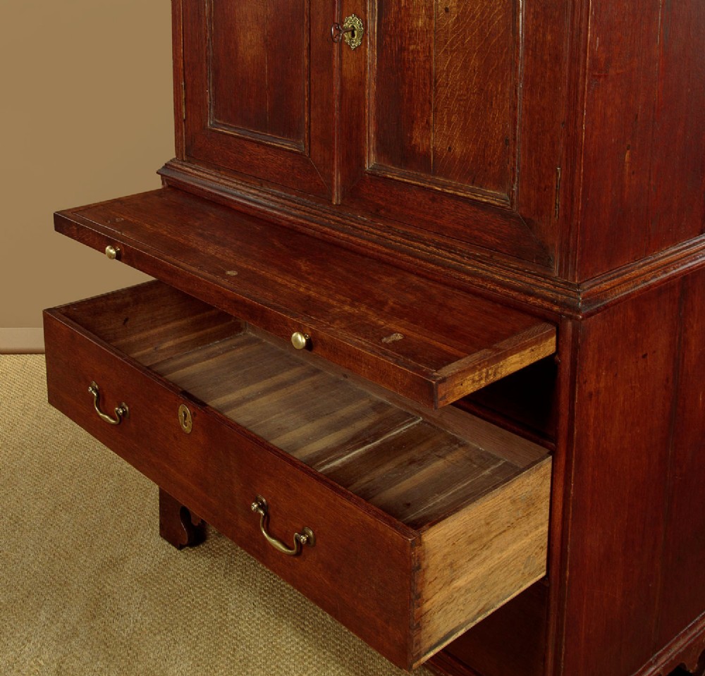 An early 18th-century oak cabinet on chest featuring twin panelled doors opening to internal drawers and pigeonholes above a chest of drawers with brass handles. View XII