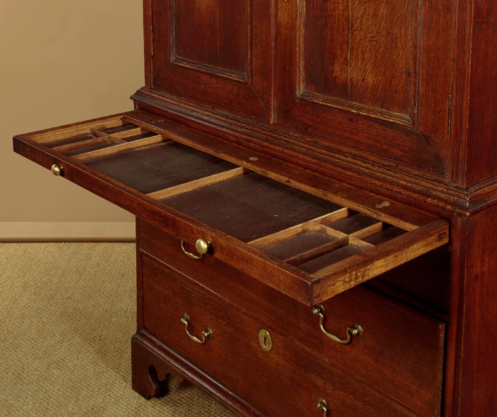 An early 18th-century oak cabinet on chest featuring twin panelled doors opening to internal drawers and pigeonholes above a chest of drawers with brass handles. View XIII