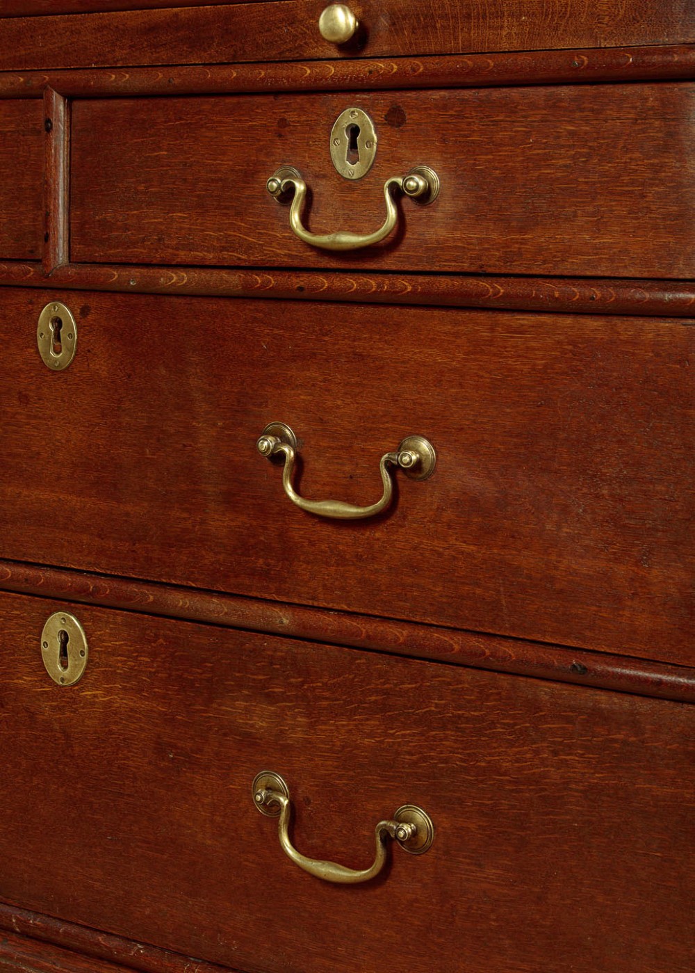 An early 18th-century oak cabinet on chest featuring twin panelled doors opening to internal drawers and pigeonholes above a chest of drawers with brass handles. View XIV