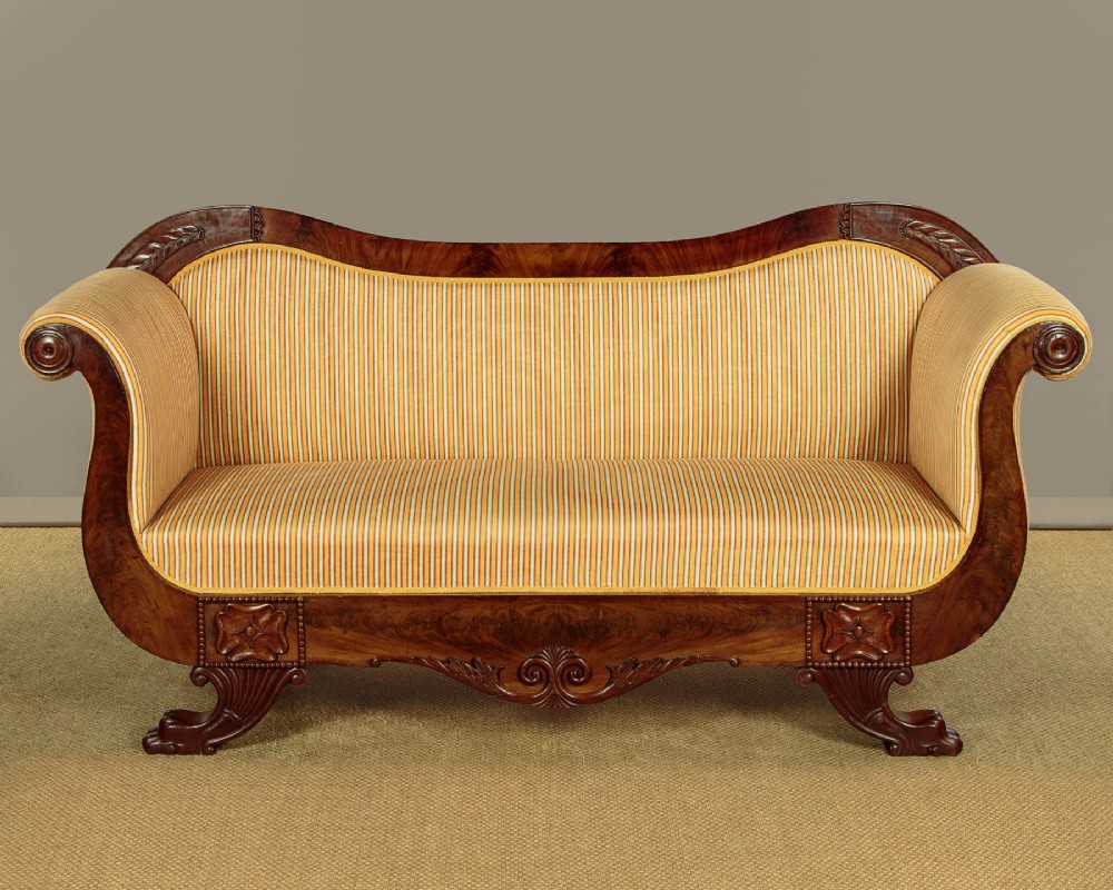 A Regency mahogany scroll end couch featuring swept arms, carved anthemion accents, and yellow striped fabric upholstery.