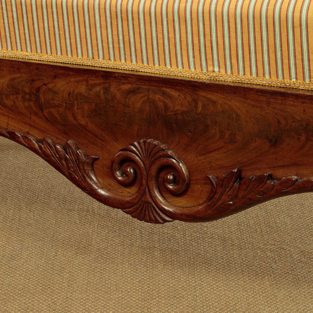 A Regency mahogany scroll end couch featuring swept arms, carved anthemion accents, and yellow striped fabric upholstery. View X