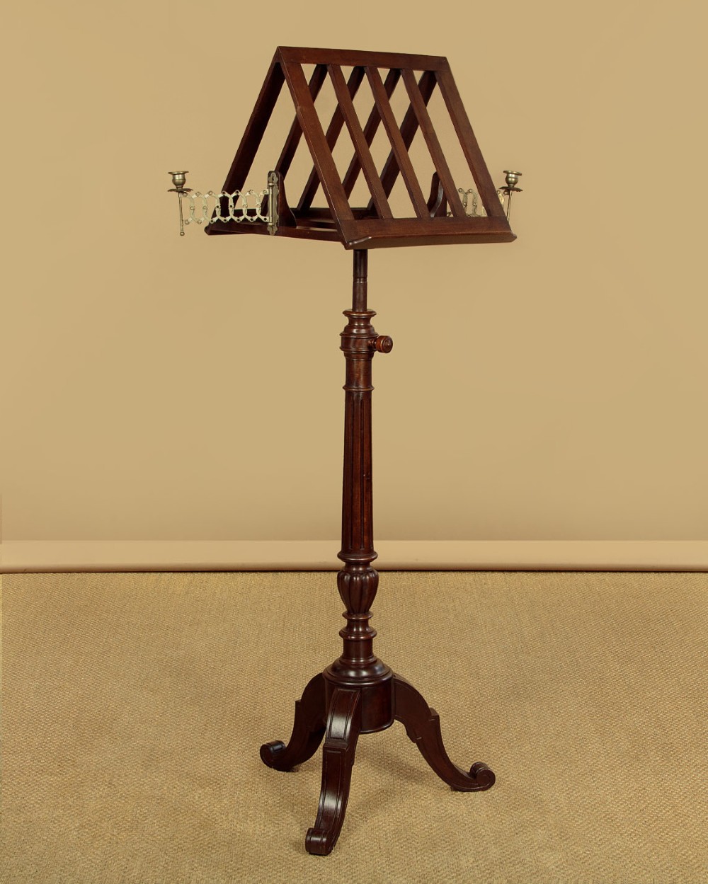 An antique dark mahogany duet music stand with a double-sided slatted rack, twin adjustable brass candle sconces, and a tripod base.