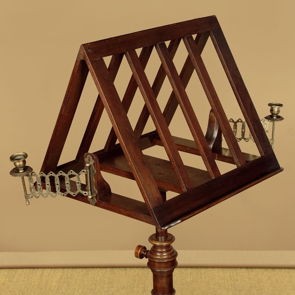 An antique dark mahogany duet music stand with a double-sided slatted rack, twin adjustable brass candle sconces, and a tripod base. View IV