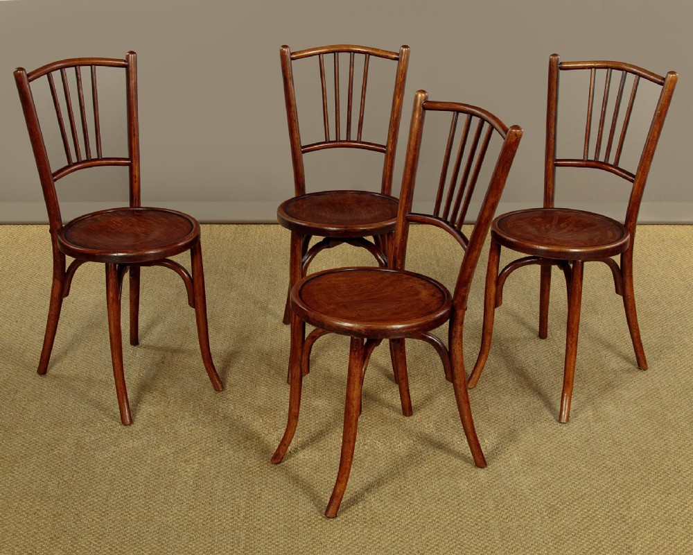 A set of four dark brown bentwood bistro dining chairs with vertical spindle backs, circular wooden seats, and curved legs.