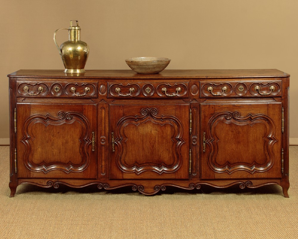 An 18th-century French provincial dark oak dresser base featuring three carved panel doors, three upper drawers with brass handles, and a shaped apron on short scrolled feet. View II