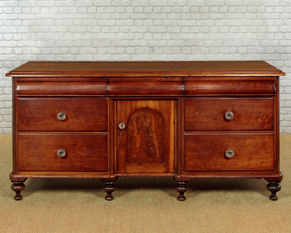 A Victorian walnut sideboard featuring a central arched cupboard door flanked by drawers with faceted glass knobs, set on turned feet.