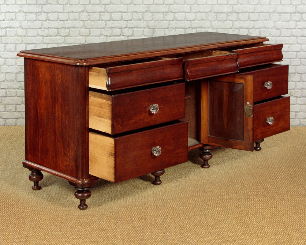 A Victorian walnut sideboard featuring a central arched cupboard door flanked by drawers with faceted glass knobs, set on turned feet. View V