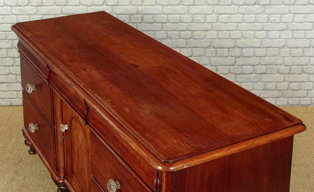 A Victorian walnut sideboard featuring a central arched cupboard door flanked by drawers with faceted glass knobs, set on turned feet. View VI