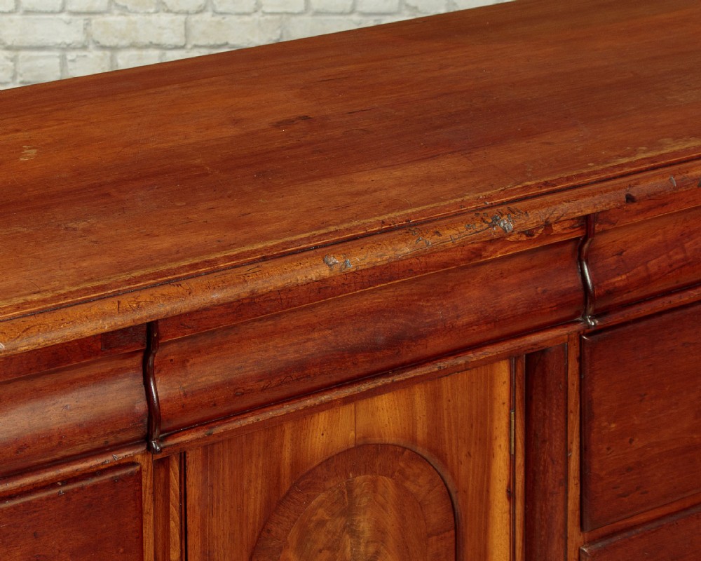 A Victorian walnut sideboard featuring a central arched cupboard door flanked by drawers with faceted glass knobs, set on turned feet. View VII