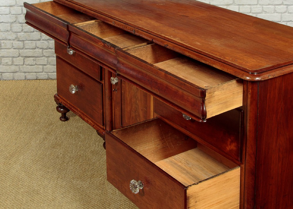 A Victorian walnut sideboard featuring a central arched cupboard door flanked by drawers with faceted glass knobs, set on turned feet. View VIII
