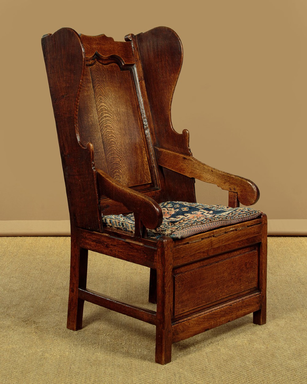 A late 18th-century dark oak lambing chair featuring high winged sides, a panelled back, a patterned seat cushion, and a drawer in the base. View II