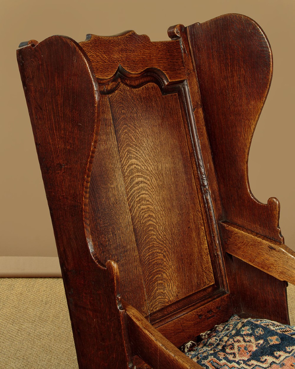 A late 18th-century dark oak lambing chair featuring high winged sides, a panelled back, a patterned seat cushion, and a drawer in the base. View IV