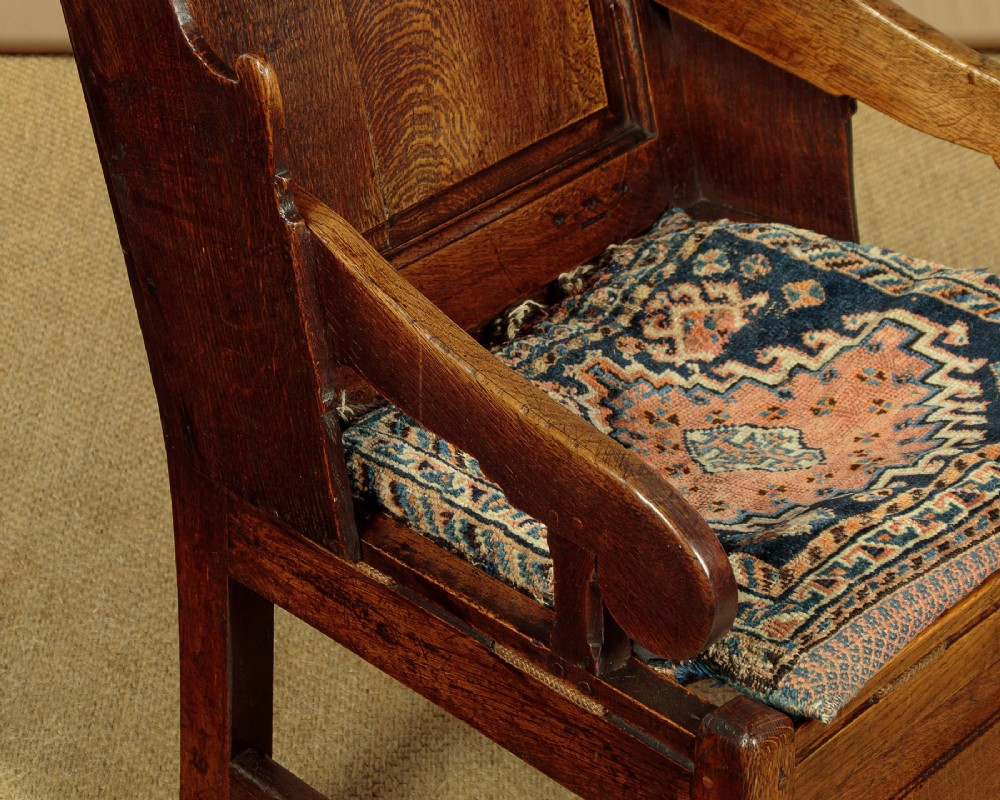 A late 18th-century dark oak lambing chair featuring high winged sides, a panelled back, a patterned seat cushion, and a drawer in the base. View VI