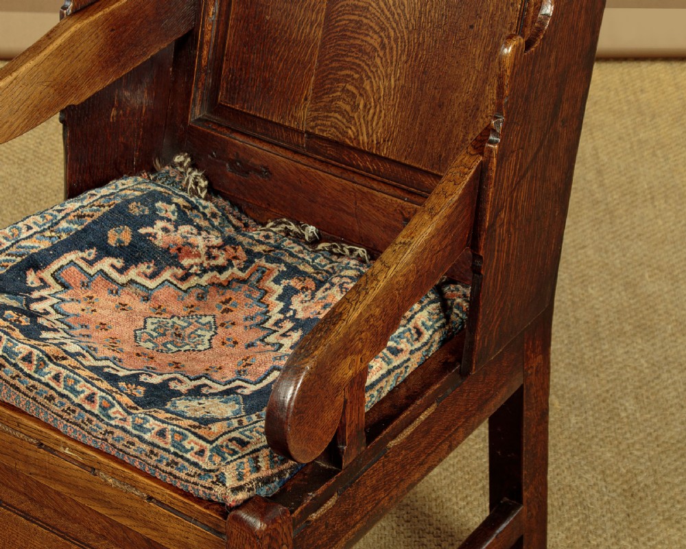 A late 18th-century dark oak lambing chair featuring high winged sides, a panelled back, a patterned seat cushion, and a drawer in the base. View VII