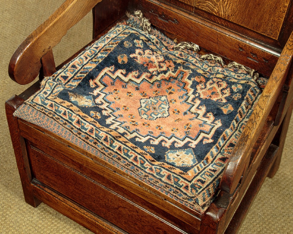 A late 18th-century dark oak lambing chair featuring high winged sides, a panelled back, a patterned seat cushion, and a drawer in the base. View VIII