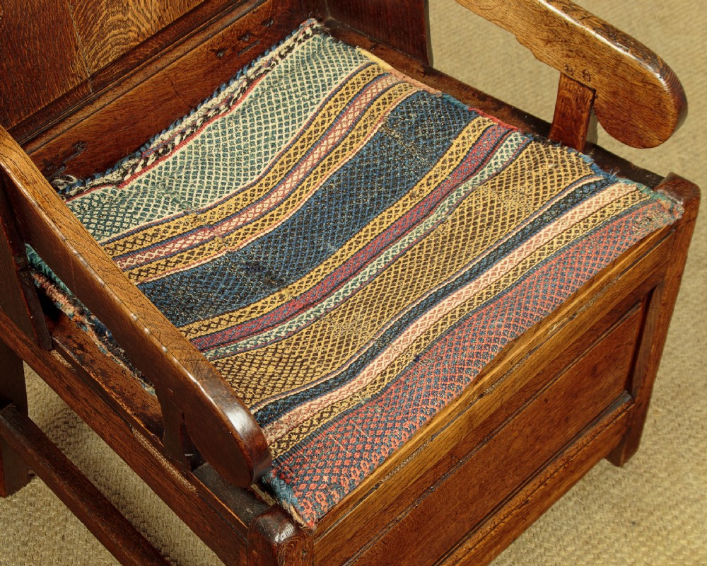 A late 18th-century dark oak lambing chair featuring high winged sides, a panelled back, a patterned seat cushion, and a drawer in the base. View IX