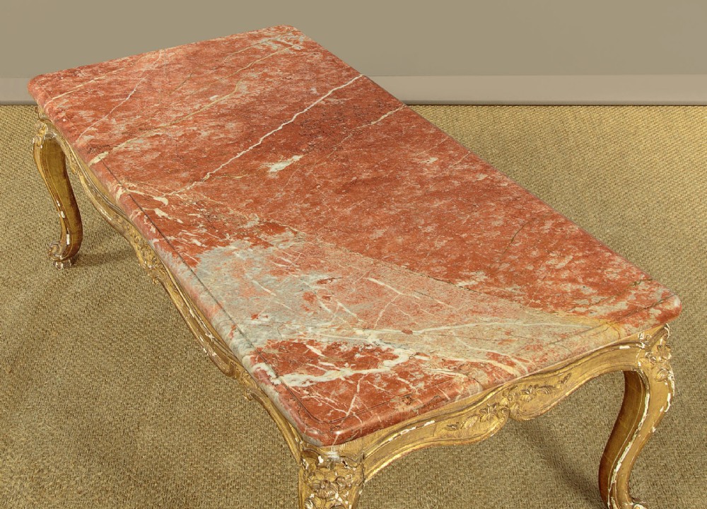 A low rectangular coffee table featuring a pink and red veined marble top supported by a carved giltwood frame with cabriole legs. View V